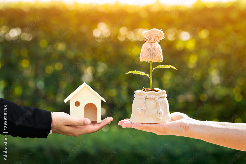 Φωτογραφία Businessman and woman hand holding a model home and money bag presenting to each other in the public park, Saving money for buy a new house or loan for plan business investment of real estate concept
