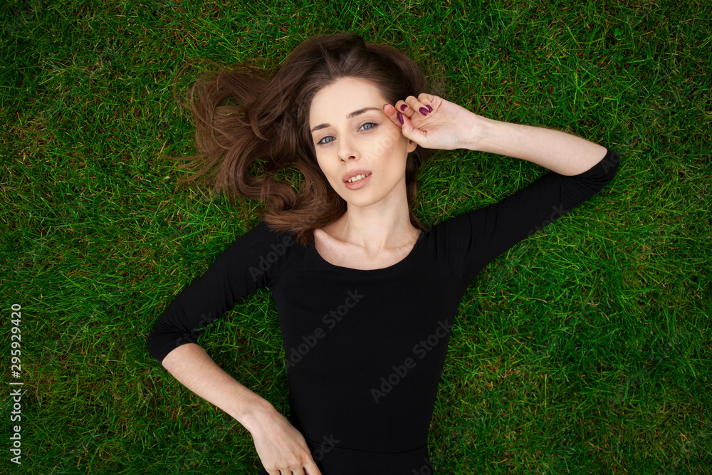 Top view portrait of a young beautiful woman in black dress lies on green lawn in a park Top view portrait of a young beautiful woman in black dress lies on green lawn in a park