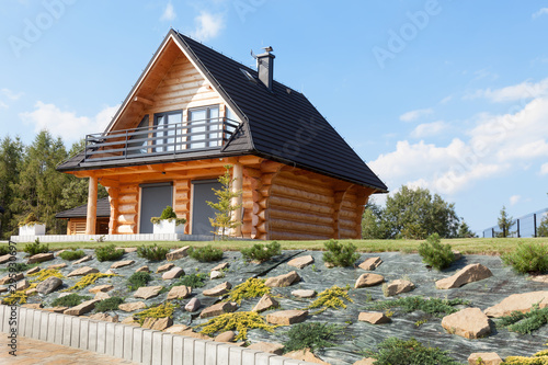 New wooden house on grassy hill, under blue sky.  House in mountains.