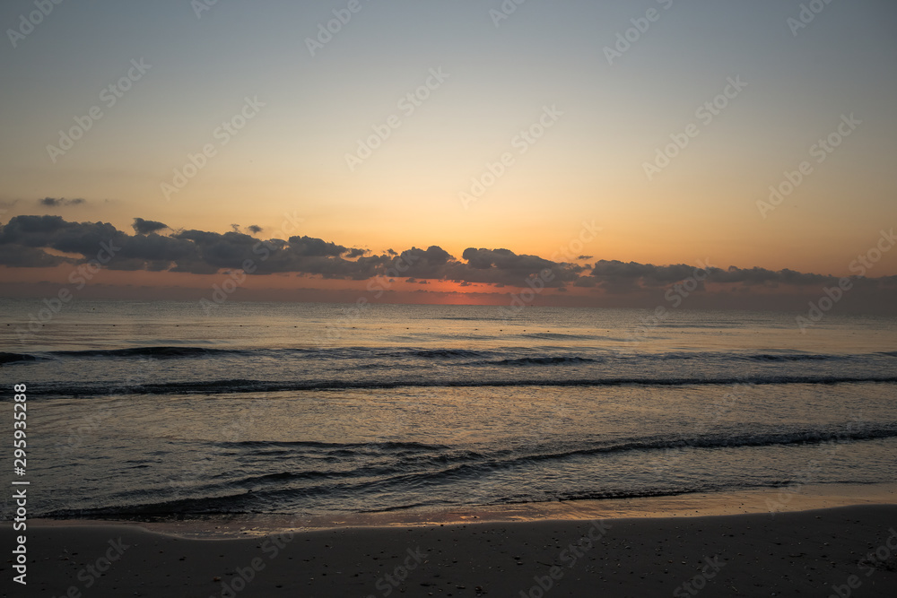 Sunrise. Dawn on the Mediterranean coast, Tunisia Sand in the foreground, small waves, the sun above the horizon, long clouds