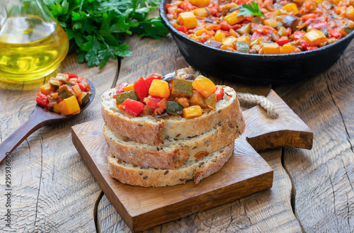 Spanish cuisine. Vegetable dish pisto manchego made of tomatoes, zucchini, bell peppers, onions and eggplant served on white bread. Wooden background.
