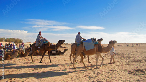 Group of tourists over dromedary camel walking in the sands