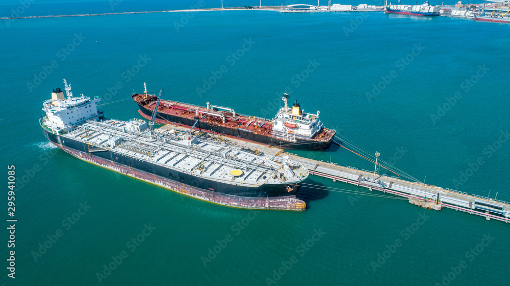 Aerial top view of fuel tanker ship at the port, Oil terminal is industrial facility for storage of oil and gas petrochemical products ready for transport to further storage facilities.