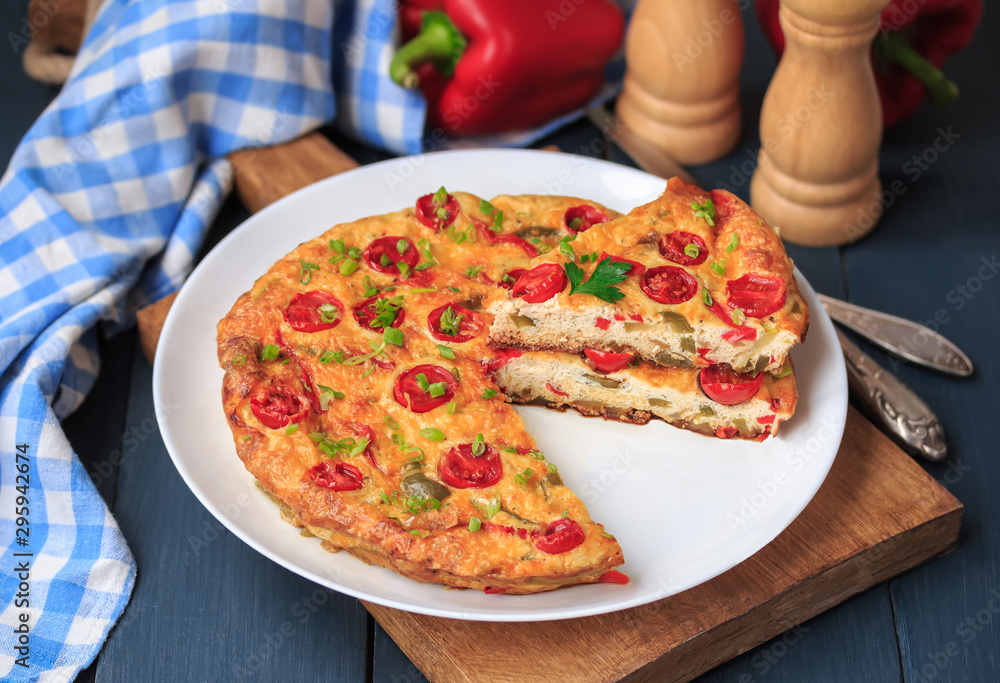 Italian omelet. Sliced vegetable frittata with onion, bell peppers, fresh herbs and cherry tomatoes. Dark background, white plate. 