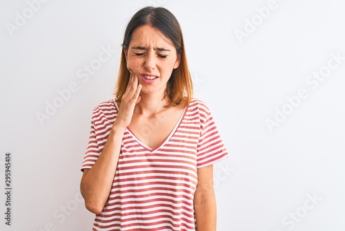 Beautiful redhead woman wearing casual striped red t-shirt over isolated background touching mouth with hand with painful expression because of toothache or dental illness on teeth. Dentist concept. © Krakenimages.com