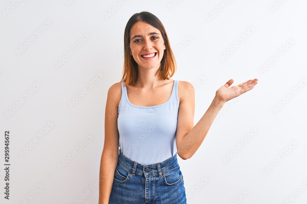 Beautiful redhead woman standing over isolated background smiling cheerful presenting and pointing with palm of hand looking at the camera. Beautiful redhead woman standing over isolated background smiling cheerful presenting and pointing with palm of hand looking at the camera.