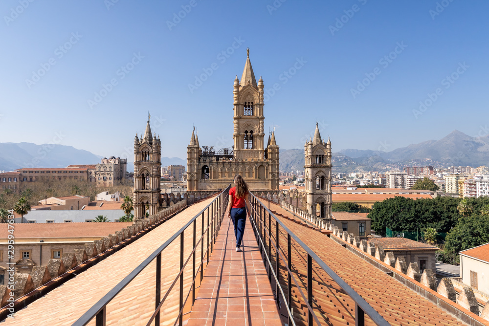 Woman tourist visitor walking on the rooftop catwalk of the Palermo Cathedral or Cattedrale di Palermo with bell towers in the background on a nice sunny afternoon in Palermo, Sicily.