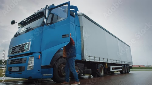 Truck Driver Crosses the Road in the Rural Area and Gets into His Blue Long Haul Semi-Truck with Cargo Trailer Attached. Logistics Company Moving Goods Across Countrie and Continent photo