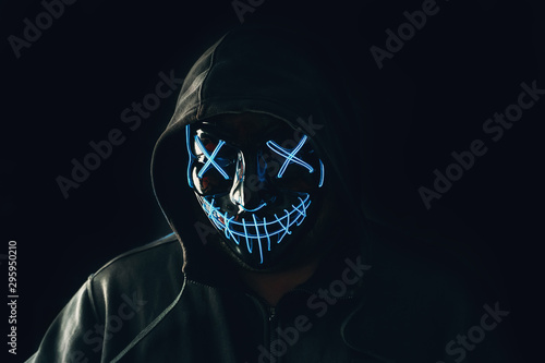 Man with lighting neon glow mask in hood on black background. Halloween and horror concept