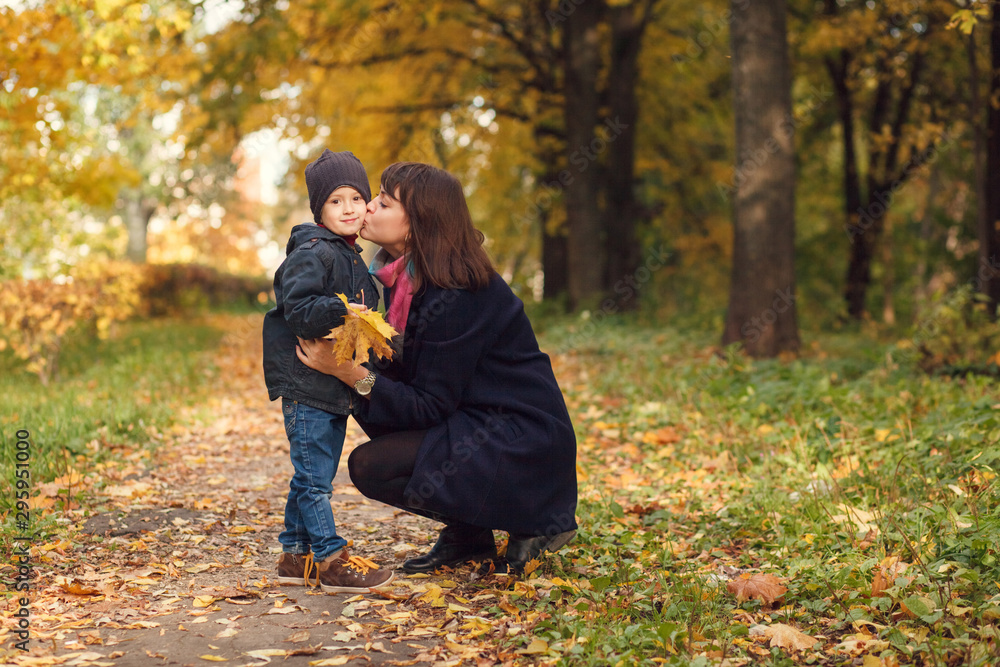 Fototapeta premium A loving mother kisses her son outdoors on a warm autumn day.