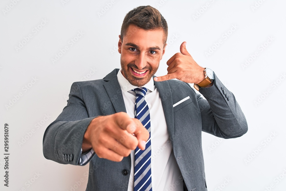Young handsome business man wearing suit and tie over isolated background smiling doing talking on the telephone gesture and pointing to you. Call me. Young handsome business man wearing suit and tie over isolated background smiling doing talking on the telephone gesture and pointing to you. Call me.