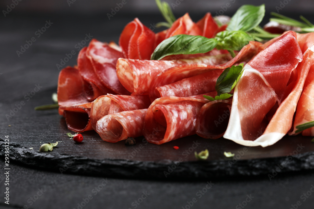 Marble cutting board with prosciutto, bacon, salami and sausages on wooden background. Rustic Meat platter