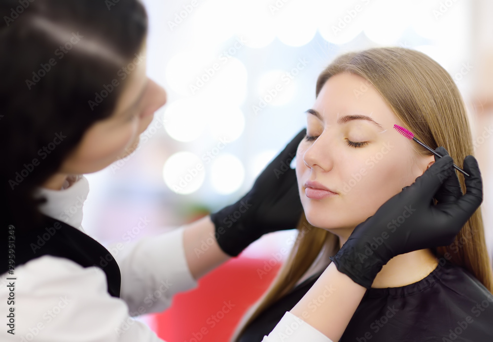 Beautician combs eyebrows using special brush on face young beautiful model. Facial care and make up Beautician combs eyebrows using special brush on face young beautiful model. Facial care and make up