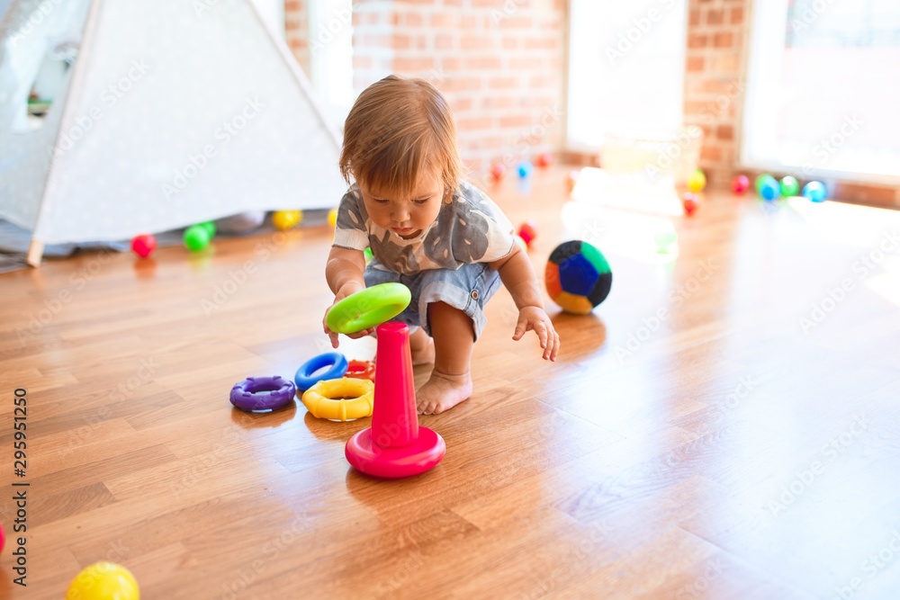 Adorable toddler building pyramid using hoops around lots of toys at kindergarten Adorable toddler building pyramid using hoops around lots of toys at kindergarten