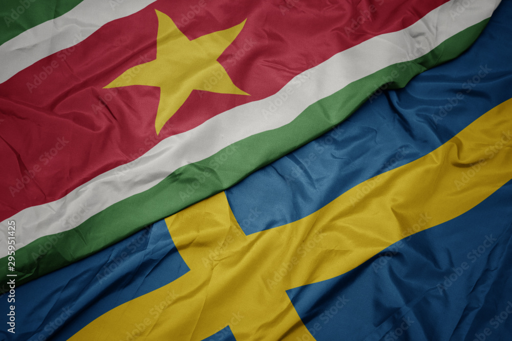 waving colorful flag of sweden and national flag of suriname.