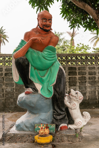 Bang Saen, Thailand - March 16, 2019: Wang Saensuk Buddhist Monastery. Colorful statue of Pra Puang To Ke, the fist Saint  with white dog, green dress under silver sky and green foliage. photo