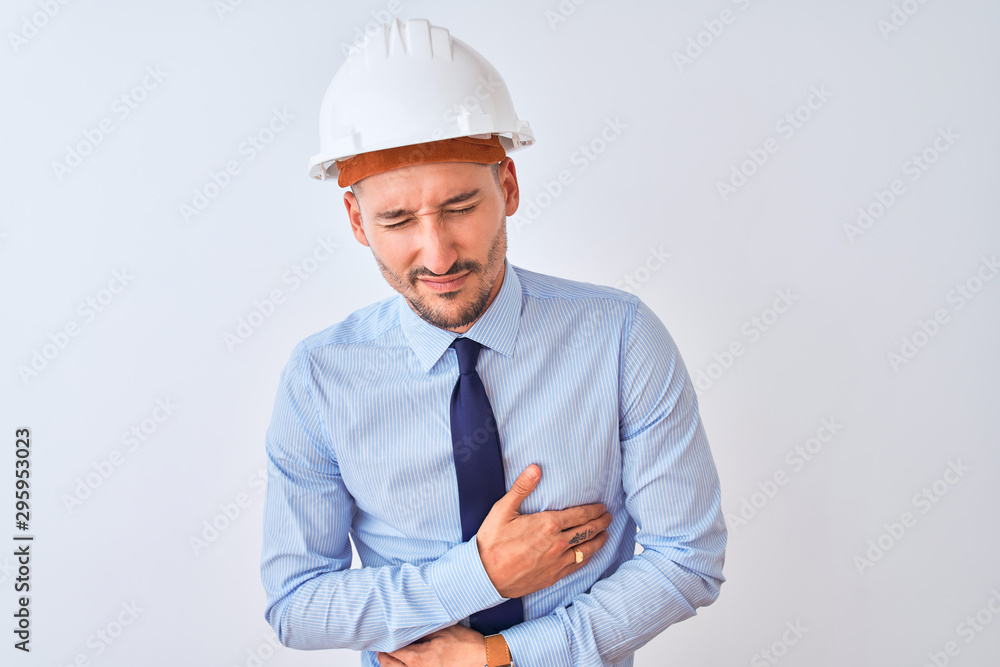 Young business man wearing contractor safety helmet over isolated background with hand on stomach because nausea, painful disease feeling unwell. Ache concept. Young business man wearing contractor safety helmet over isolated background with hand on stomach because nausea, painful disease feeling unwell. Ache concept.