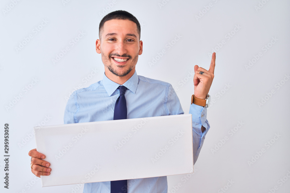 Young business man holding blank banner over isolated background very happy pointing with hand and finger to the side Young business man holding blank banner over isolated background very happy pointing with hand and finger to the side