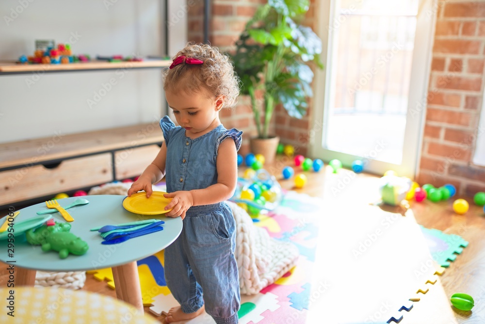 Beautiful caucasian infant playing with toys at colorful playroom. Happy and playful cooking in fake kitchen at kindergarten.
