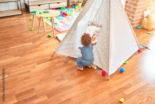 Beautiful caucasian infant playing with toys at colorful playroom. Happy and playful with indian tent at kindergarten.