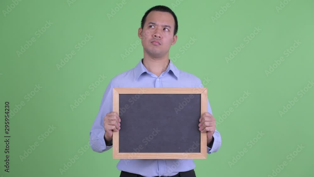 Happy Asian businessman thinking while holding blackboard Happy Asian businessman thinking while holding blackboard