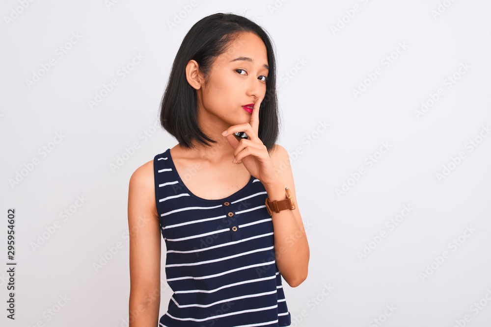 Young chinese woman wearing striped t-shirt standing over isolated white background asking to be quiet with finger on lips. Silence and secret concept. Young chinese woman wearing striped t-shirt standing over isolated white background asking to be quiet with finger on lips. Silence and secret concept.