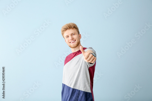Portrait of young man showing thumb-up gesture on color background