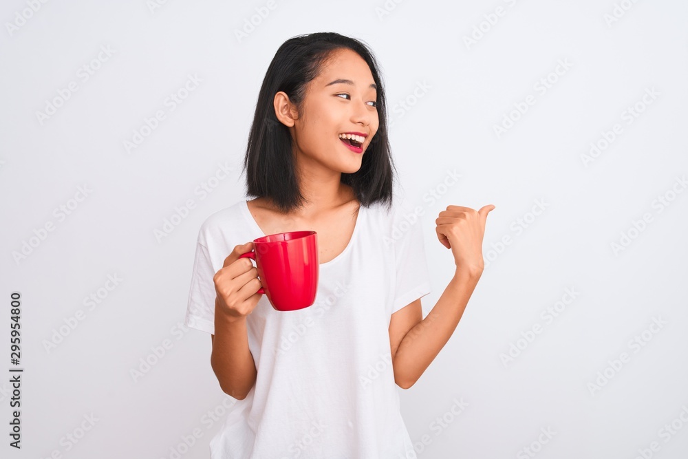 Young beautiful chinese woman drinking cup of coffee over isolated white background pointing and showing with thumb up to the side with happy face smiling Young beautiful chinese woman drinking cup of coffee over isolated white background pointing and showing with thumb up to the side with happy face smiling