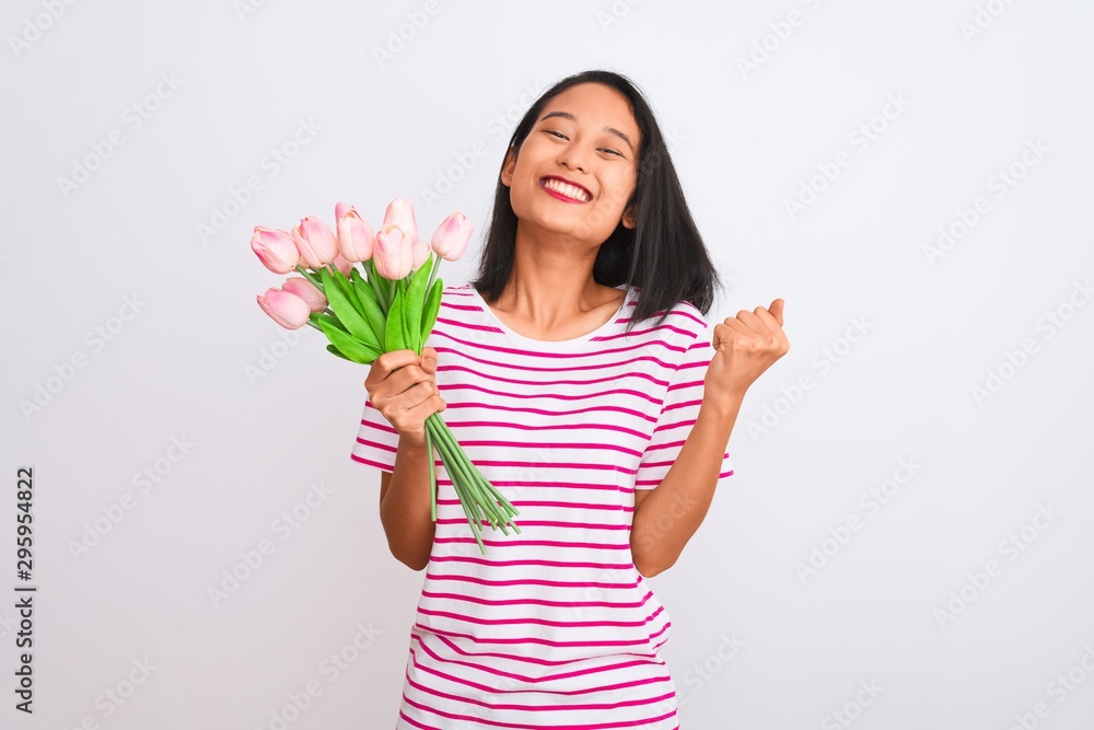 Young chinese woman holding bouquet of roses standing over isolated white background screaming proud and celebrating victory and success very excited, cheering emotion Young chinese woman holding bouquet of roses standing over isolated white background screaming proud and celebrating victory and success very excited, cheering emotion