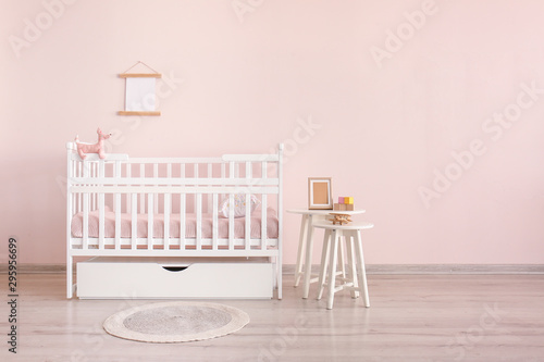 Stylish baby bed with table near color wall in interior of children's room