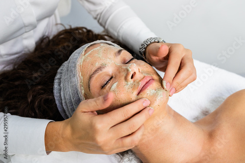 Beautiful woman receiving natural green peel facial mask with rejuvenating effects in spa beauty salon. photo