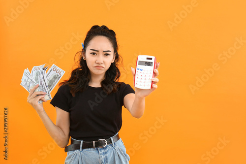 Sad Asian woman with money and calculator on color background
