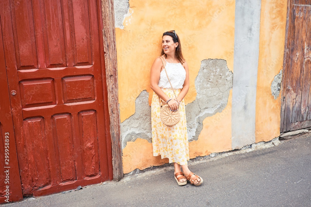 Fototapeta premium Beautiful girl leaning on orange wall, young friendly woman smiling happy on a sunny day of summer