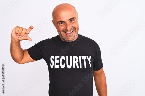 Middle age safeguard man wearing security uniform standing over isolated white background smiling and confident gesturing with hand doing small size sign with fingers looking and the camera
