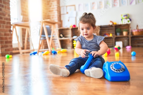 Beautiful toddler sitting on the floor playing with vintage phone at kindergarten