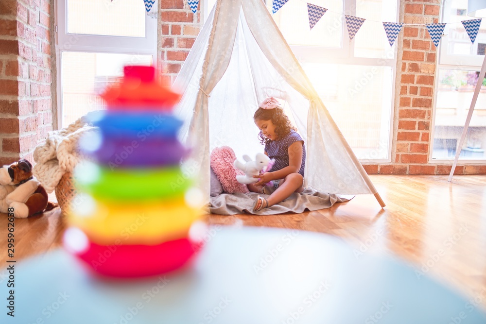 Beautiful toddler girl sitting on the floor playing with unicorn inside tipi at kindergarten
