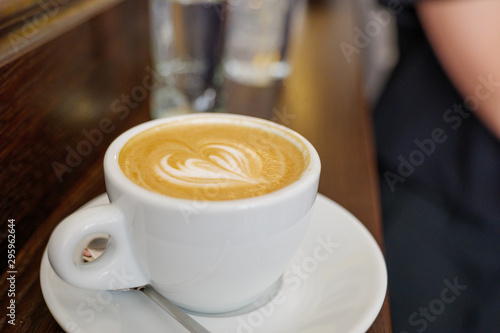 Close up and top view of beautiful latte art with heart pattern on top of coffee cappuccino in white ceramic cup on wood counter in coffee bar.