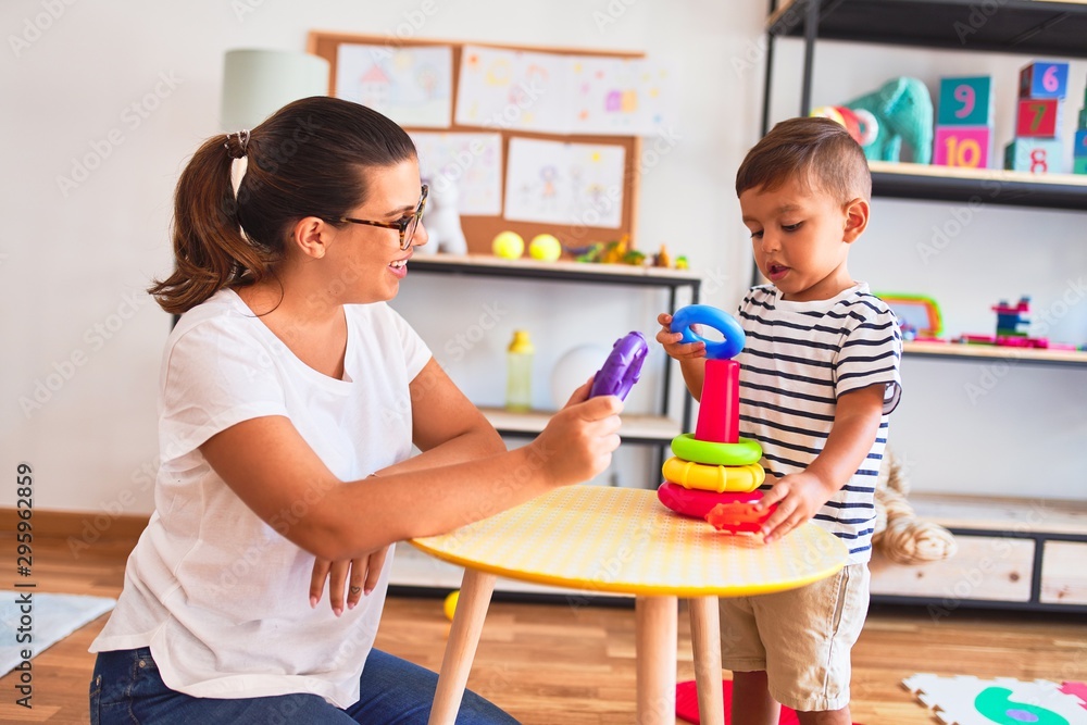 Beautiful teacher and toddler boy building pyramid with hoops bolcks at kindergarten
