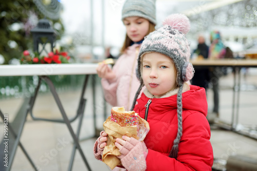 Two cute young sisters eating Czech trdelnik on traditional Christmas fair in Vilnius  Lithuania. Children enjoying sweets  candies and gingerbread on Xmas market.