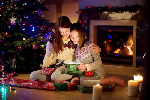 Happy young mother and her young daughter opening a magical Christmas gift by a fireplace in a cozy dark living room on Christmas eve. © MNStudio