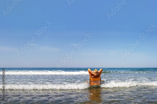 Not a young woman sitting in the sea waves in a yellow chair; rest on the Mediterranean coast in Israel; relax by the sea; contemplation of the sea waves; tourist enjoys relaxation by the sea