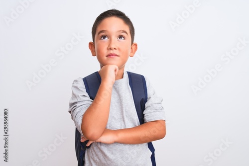 Beautiful student kid boy wearing backpack standing over isolated white background with hand on chin thinking about question, pensive expression. Smiling with thoughtful face. Doubt concept.