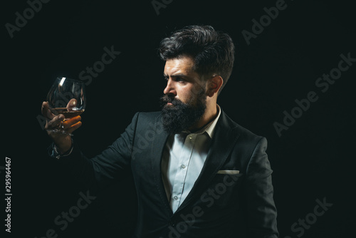 Drinking whiskey or brandy or cognac. Elegant and stylish man in classical wear holding glass with wiskey in hand. Stylish rich man holding a glass of old whisky.