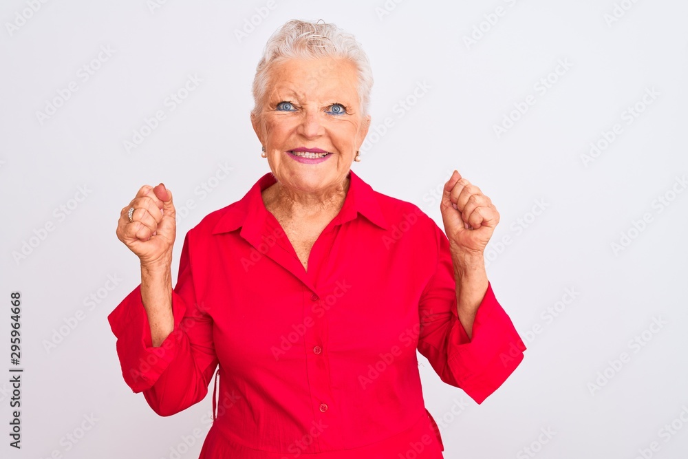 Senior grey-haired woman wearing red casual shirt standing over isolated white background excited for success with arms raised and eyes closed celebrating victory smiling. Winner concept. Senior grey-haired woman wearing red casual shirt standing over isolated white background excited for success with arms raised and eyes closed celebrating victory smiling. Winner concept.