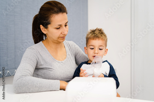 Woman mother hold her small son boy child using vapor steam inhaler nebulizer mask inhalation at home or hospital medical procedure medicament treatment asthma pneumonia bronchitis coughing sick © Miljan Živković