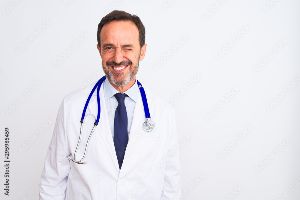 Fototapeta premium Middle age doctor man wearing coat and stethoscope standing over isolated white background winking looking at the camera with sexy expression, cheerful and happy face.