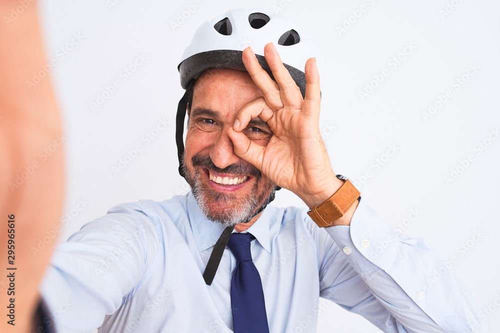 Middle age businessman wearing bike helmet make selfie over isolated white background with happy face smiling doing ok sign with hand on eye looking through fingers