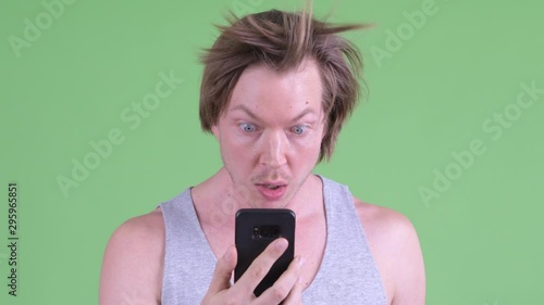 Face of funny young man using phone and looking surprised with hair blown away