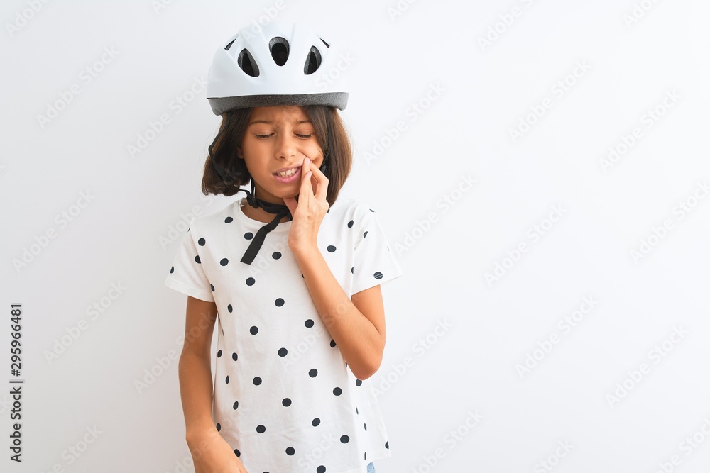 Beautiful child girl wearing security bike helmet standing over isolated white background touching mouth with hand with painful expression because of toothache or dental illness on teeth Beautiful child girl wearing security bike helmet standing over isolated white background touching mouth with hand with painful expression because of toothache or dental illness on teeth
