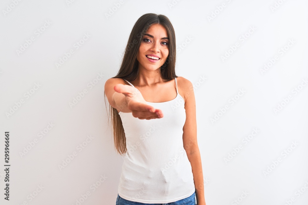 Young beautiful woman wearing casual t-shirt standing over isolated white background smiling friendly offering handshake as greeting and welcoming. Successful business. Young beautiful woman wearing casual t-shirt standing over isolated white background smiling friendly offering handshake as greeting and welcoming. Successful business.